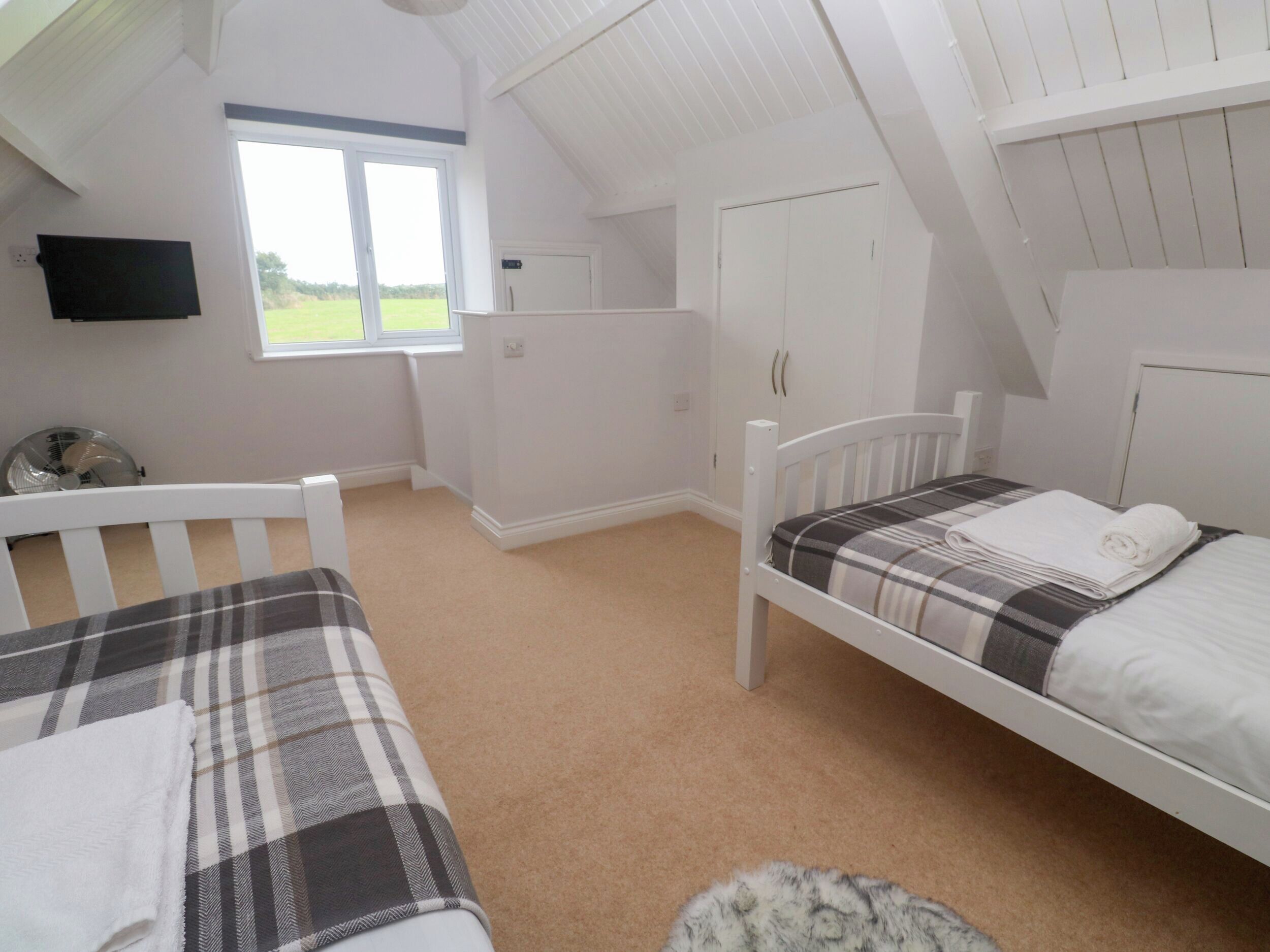 A bedroom with two beds, a window, a wardrobe, and a flat-screen TV.