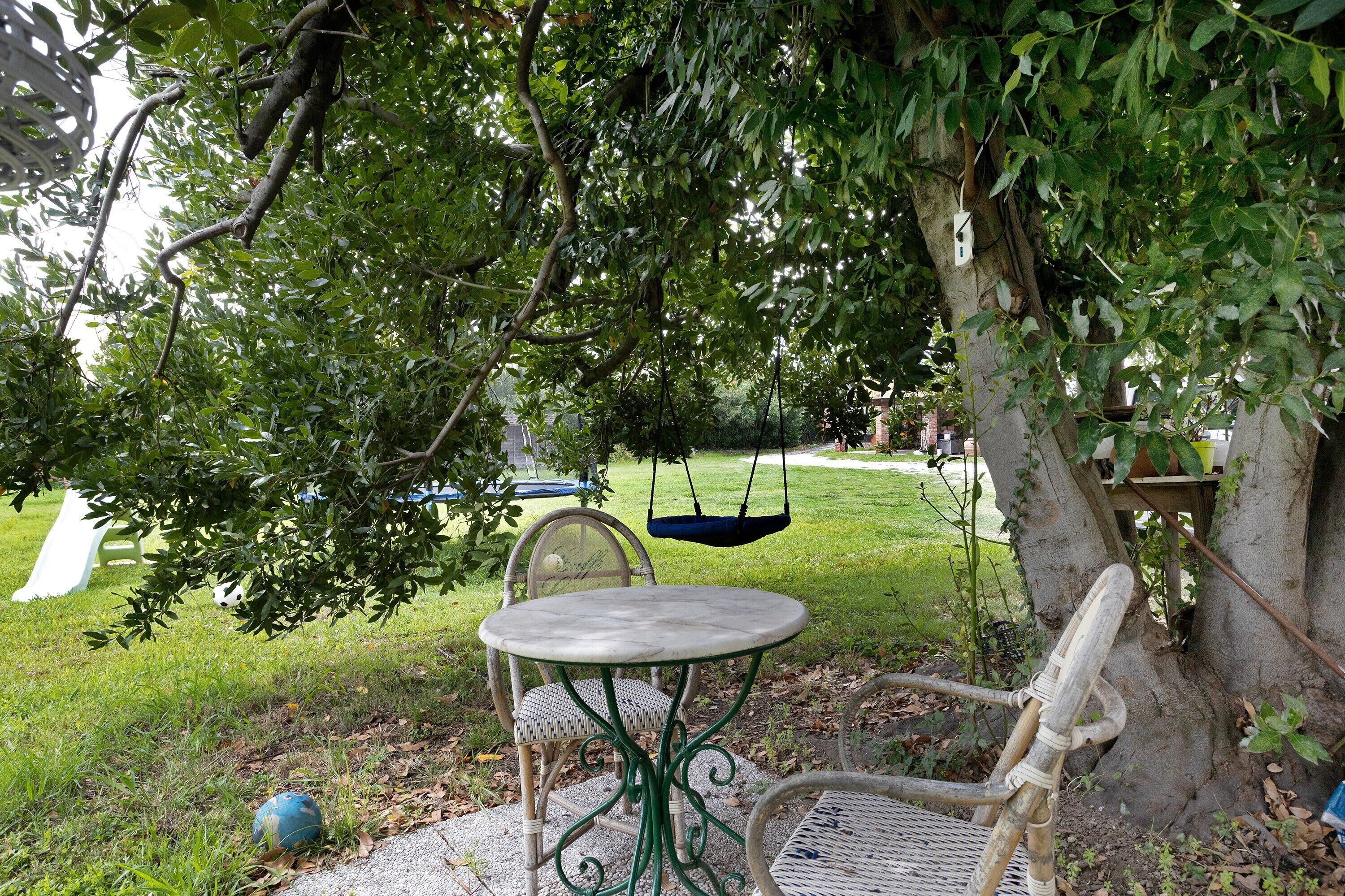 Zona de jardí amb taula i cadires, un bressol i un arbre.