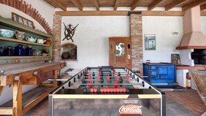 Ein Zimmer mit einem Kicker, einem mit Coca-Cola gekennzeichneten Kühlschrank, einem Kamin aus Ziegeln und einer Holzbalkendecke.