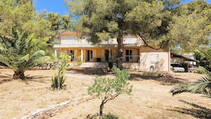 Une maison à deux étages avec un porche abrité, entourée d’arbres et d’herbe sèche.