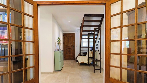 Un couloir avec un escalier, une porte en bois et une petite armoire ornée d’une plante.