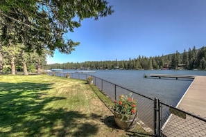 A waterfront property with a wooden deck, a fenced area with potted plants, and a view of a lake surrounded by trees.