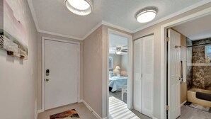 A hallway with a door, a mirror, and a bathroom with a bathtub and shower.