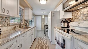 A modern kitchen with white cabinetry, a marble countertop, a built-in oven, and a microwave.