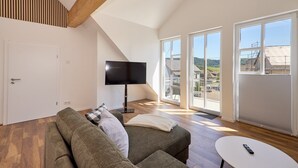 A modern living room with a sofa, a flat-screen TV, and a balcony with large windows. - Moselquartier "Winzer-Residenz" up to 8 persons | 2 balconies | box-spring beds (Piesport)