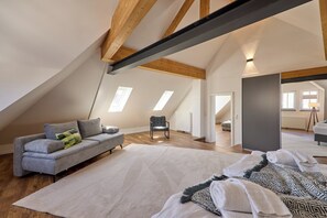 Ein Schlafzimmer im Loft-Stil mit schrägem Dach, einem grauen Sofa, einem gemusterten Teppich und einem großen Fenster.