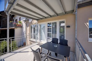 Ein Balkon mit Tisch, Stühlen, Geländer und Topfpflanzen.