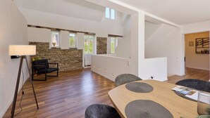 A modern dining area with a wooden table, grey upholstered chairs, and a stone accent wall. - Moselquartier "Winzer-Residenz" up to 8 persons | 2 balconies | box-spring beds (Piesport)