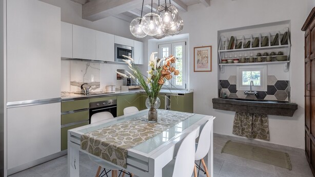 Una cocina moderna con armarios blancos, un protector contra salpicaduras de mármol y una zona de comedor con mesa de cristal.