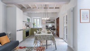 Una cocina moderna con armarios blancos, un comedor con una mesa preparada para cuatro personas y una sala de estar con sofá y alfombra.