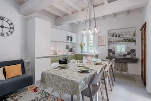 A modern kitchen with white cabinets, a dining table set for four, and a clock on the wall. - Charming Tuscan Stone House - Near Lucca (Pescaglia)