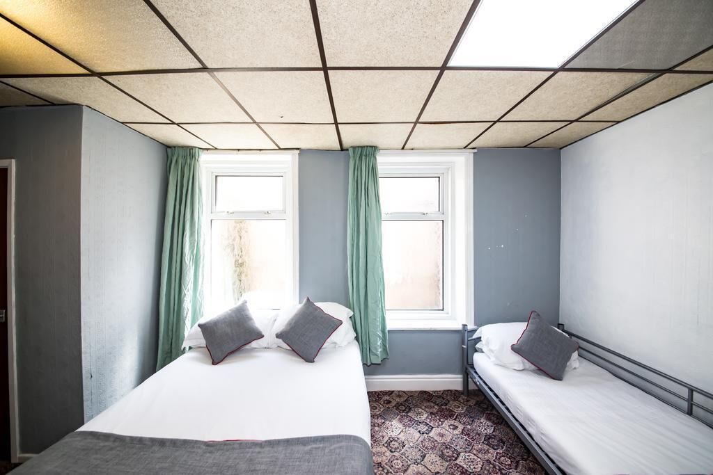 A room with a bed, a smaller bed, and a window with curtains.