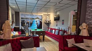 A cozy indoor space with red upholstered seating, a pool table, and a Christmas tree. - MyRoomz Silver Strand Hotel (Blackpool)