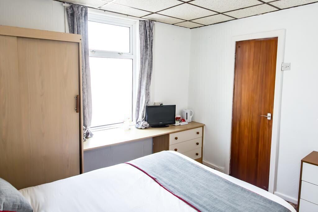 Un dormitorio con cama, un armario de madera, un escritorio con televisor y una puerta.