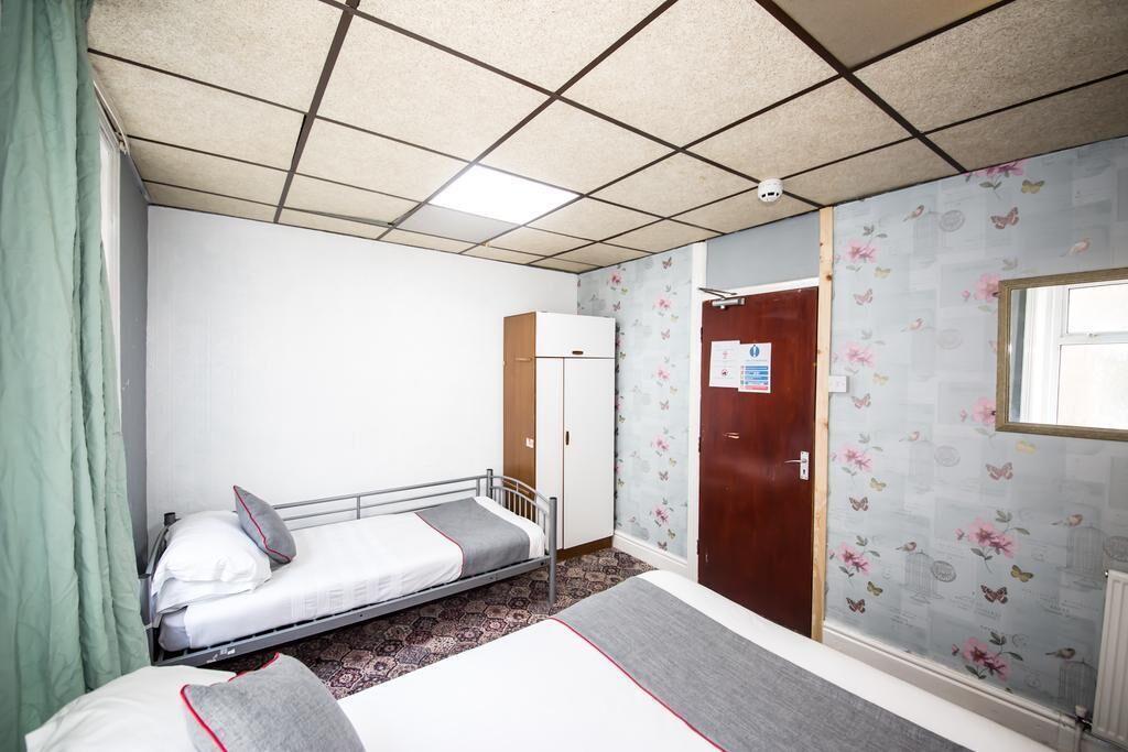 A small, single-bed room with a bunk bed, a wardrobe, a door with a sign, and patterned wallpaper.