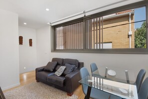 Ein modernes Wohnzimmer mit einem Glastisch, einer Ledersofa und einem großen Fenster mit Jalousien.