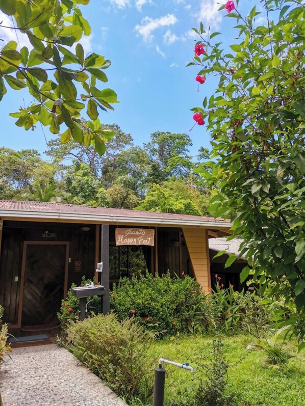 A rustic building with a 'Welcome' sign and a 'Happy Feet' sign, surrounded by lush greenery and a clear blue sky. - Casita y Tours Happy Feet Drake Bay - Room #1 (Puntarenas Province)