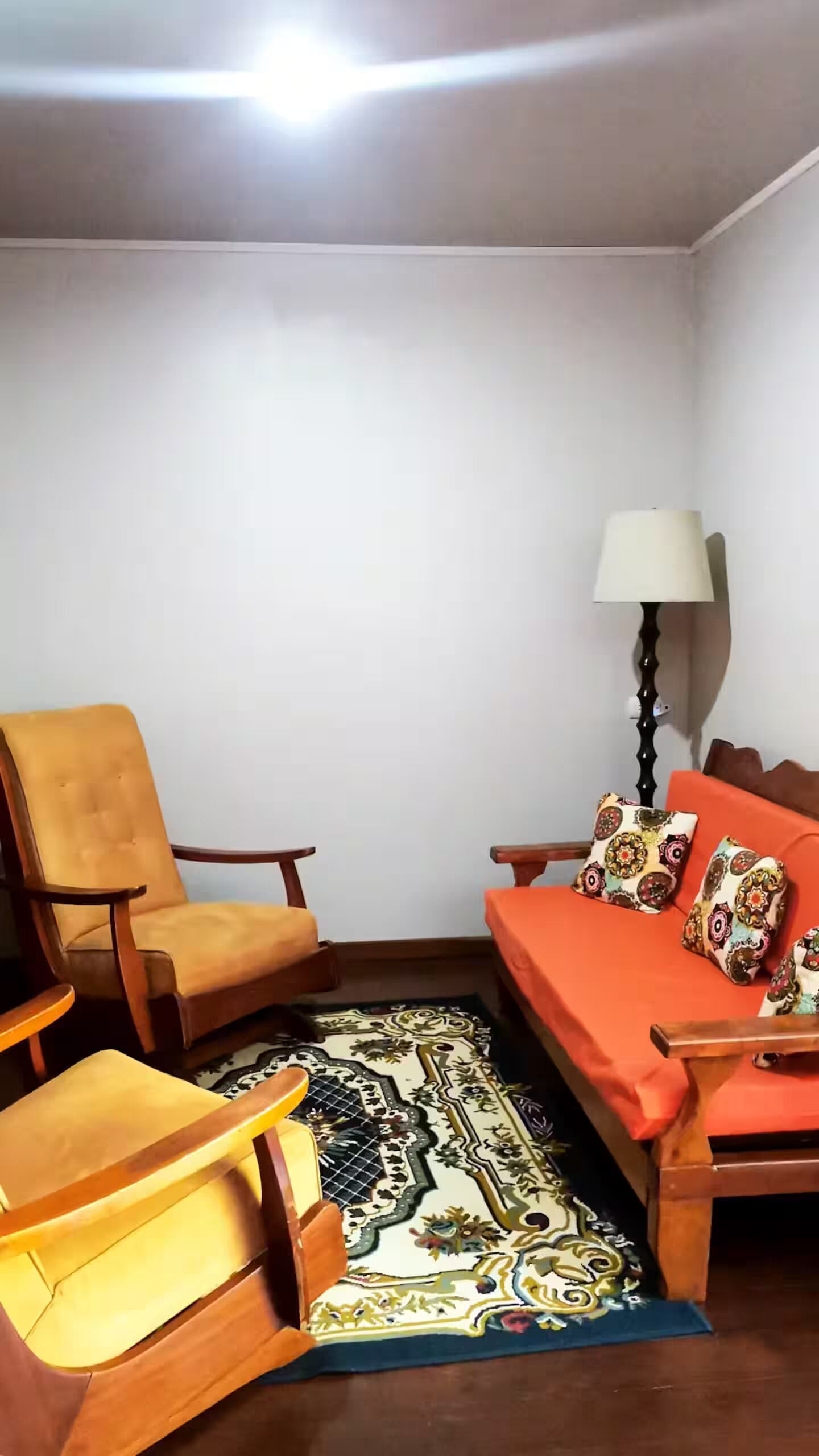 A small, cozy room with a sofa, two chairs, a patterned rug, and a lamp.