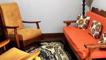 A small, cozy room with a sofa, two chairs, a patterned rug, and a lamp.
