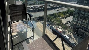 A balcony with a glass table and chairs, overlooking a cityscape with buildings and a highway. - 2-bdr 1 bath downtown  luxury condo, free parking sleeps 6 (Toronto)