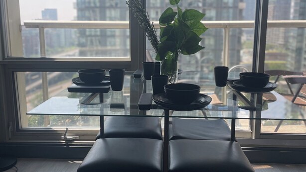 A modern dining area with a glass table, black chairs, and a potted plant. - 2-bdr 1 bath downtown  luxury condo, free parking sleeps 6 (Toronto)