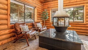 A log cabin interior with a fireplace, leather chairs, and large windows offering a forest view. - Lodge Hot Tub Dueling Basketball (Park City)