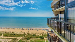 A beach view from a balcony with a clear sky, a sandy beach, and umbrellas. - Sea Watch- Penthouse, Oceanfront 4 BR, two floors (Ocean City)