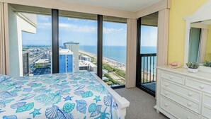 A hotel room with a large bed, a dresser, and a view of the beach and cityscape. - Sea Watch- Penthouse, Oceanfront 4 BR, two floors (Ocean City)