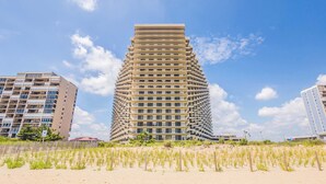 A tall, modern building with a unique stepped design, surrounded by a sandy beach and other buildings. - Sea Watch- Penthouse, Oceanfront 4 BR, two floors (Ocean City)
