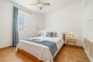 Una camera da letto con un letto, un comodino, una ventola a soffitto, una finestra con tende e vista sull'esterno.