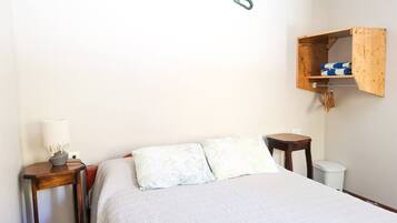 Een slaapkamer met een bed, een nachtkastje, een lamp, een houten plank en een haak aan de muur.