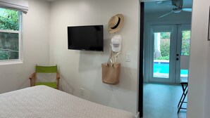 Quarto com uma cama, televisão, cadeira, chapéu e uma sacola de lona na parede.