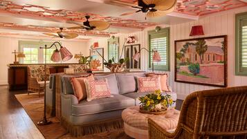 A room with a grey sofa, wicker chairs, a ceiling fan, and a painting on the wall.