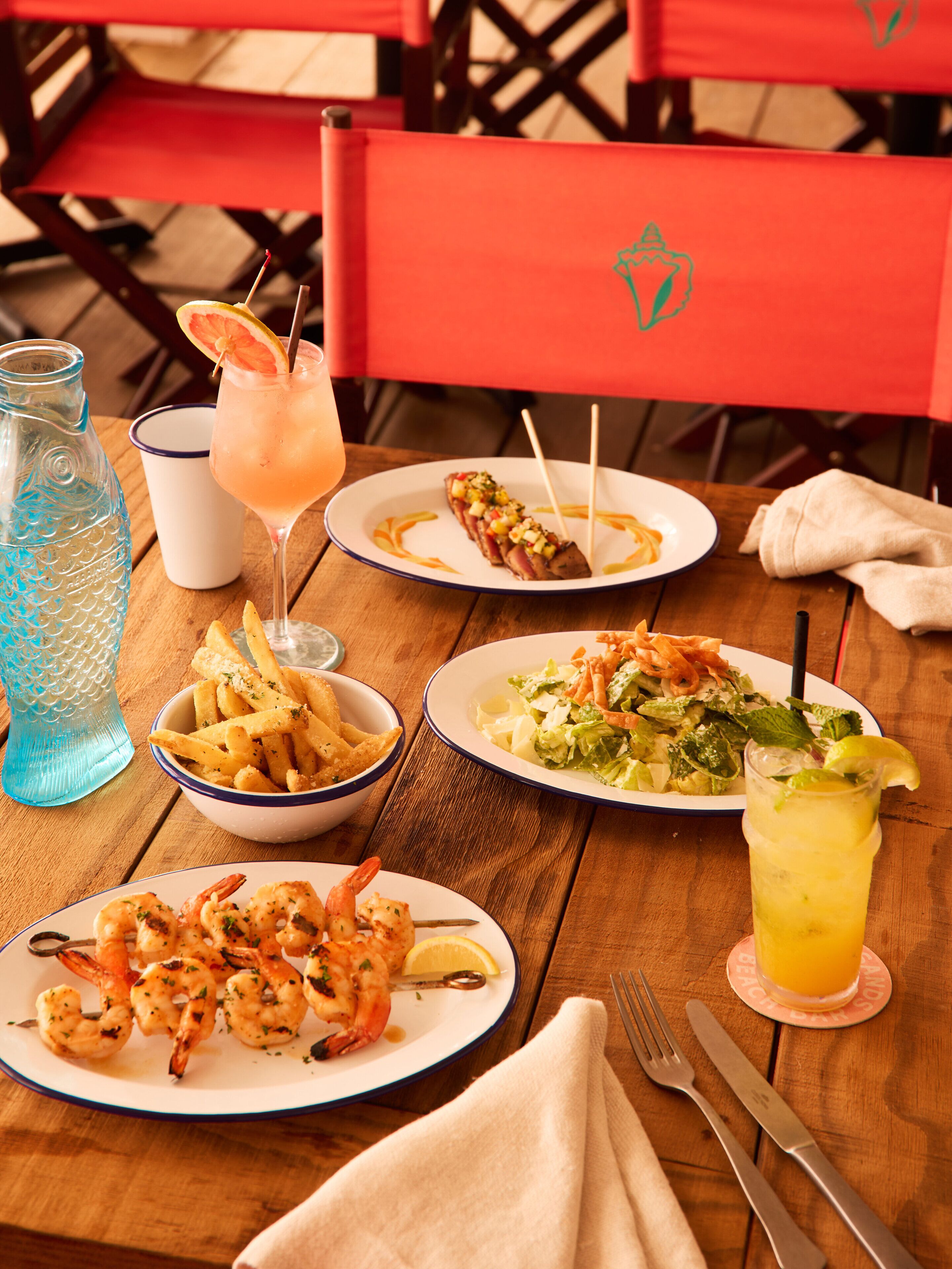 A wooden table with plates of food, a drink, and a water bottle.