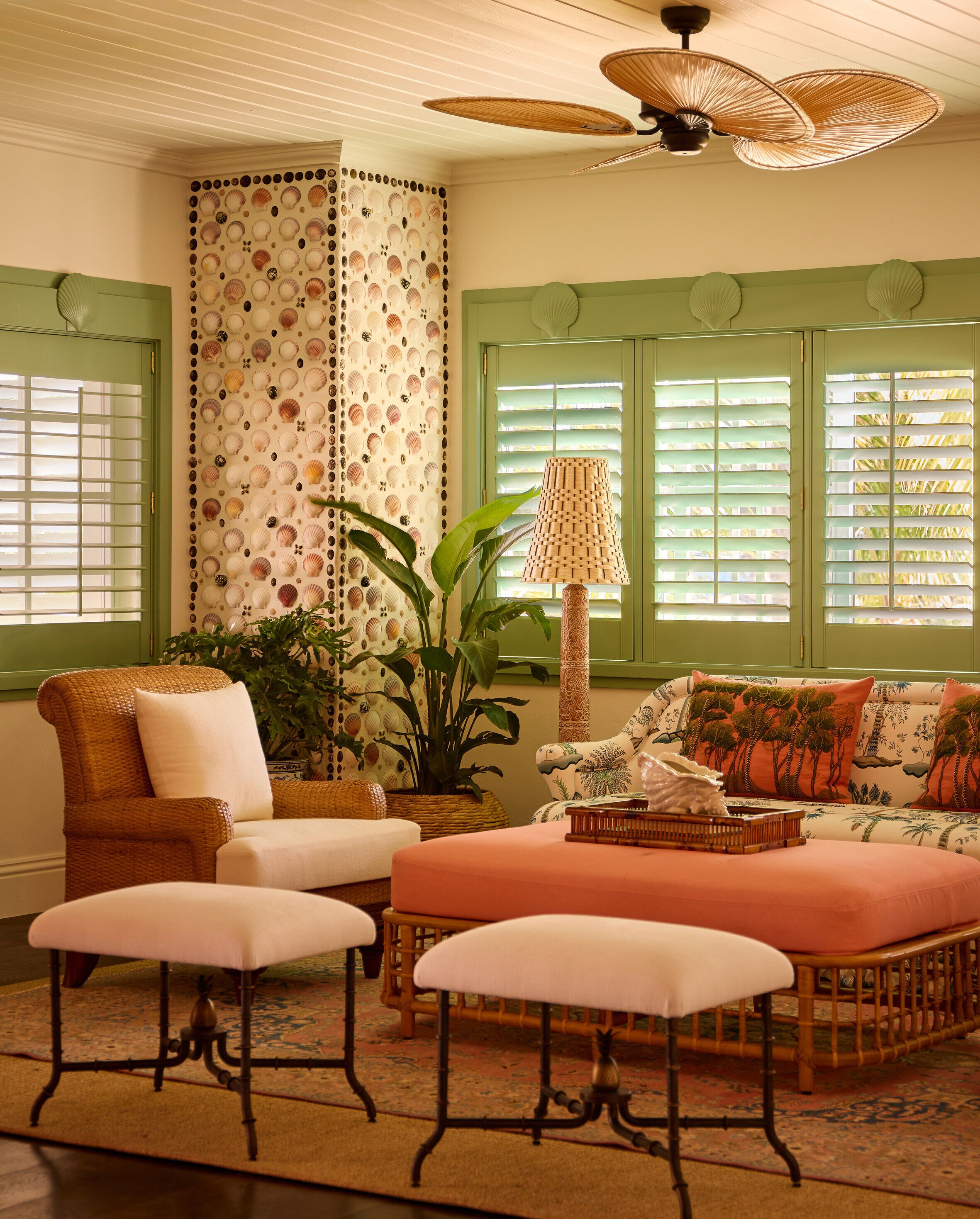 A room with a wicker sofa, a matching armchair, and a cushioned bench. There is a large potted plant and a floor lamp.