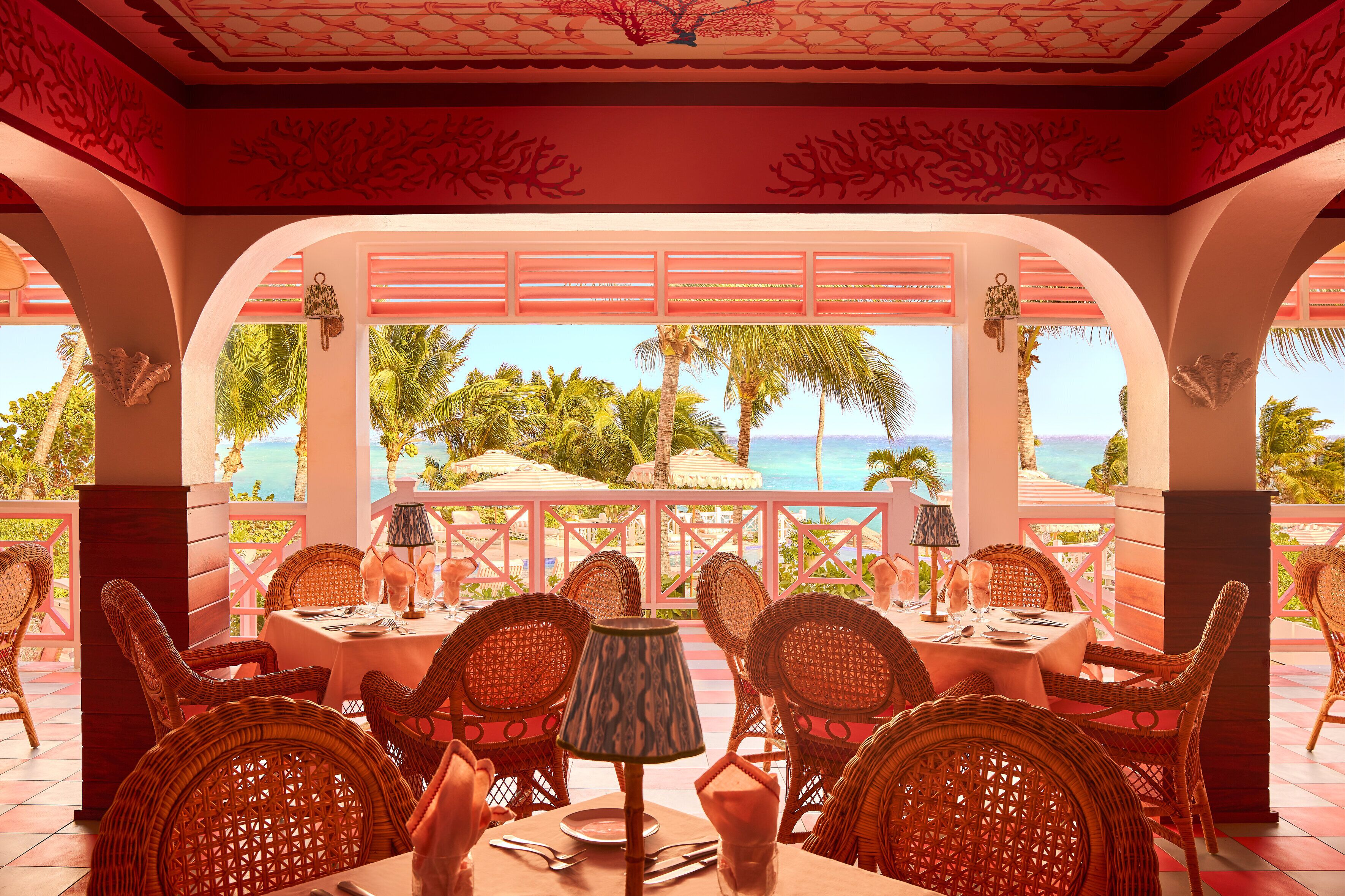 A dining area with wicker chairs, a table set for two, and a view of palm trees and the sea.