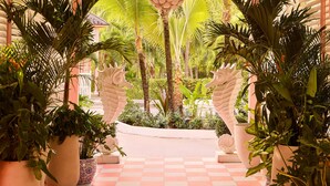 A covered walkway with a checkered floor, surrounded by potted plants and palm trees, leading to a central area with a decorative ceiling feature. - Private Pool Villa at Coral Sands Steps to Pink Sand Beach & Resort Amenities (Dunmore Town)