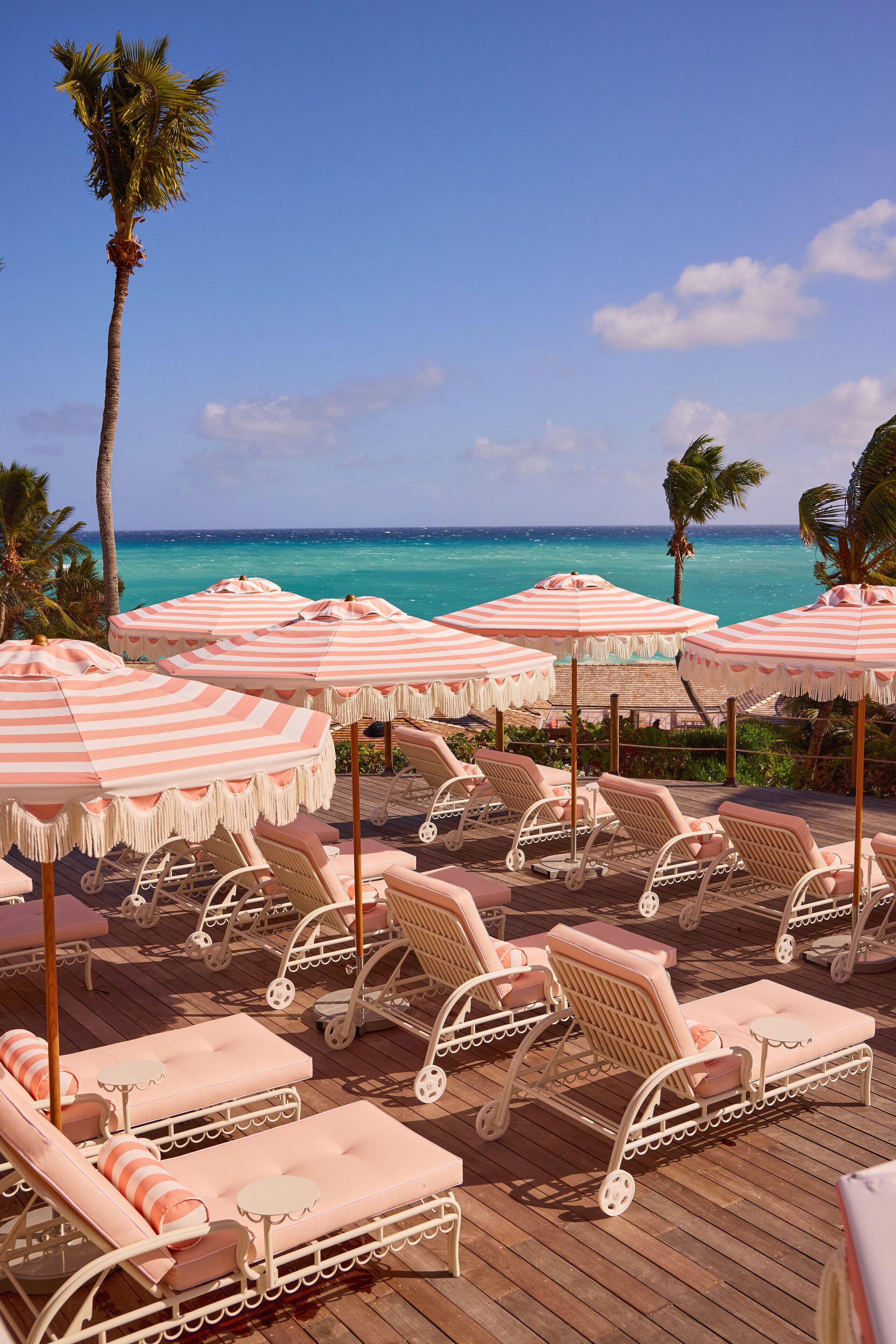 A beachside lounge area with striped umbrellas, lounge chairs, and a view of the ocean.