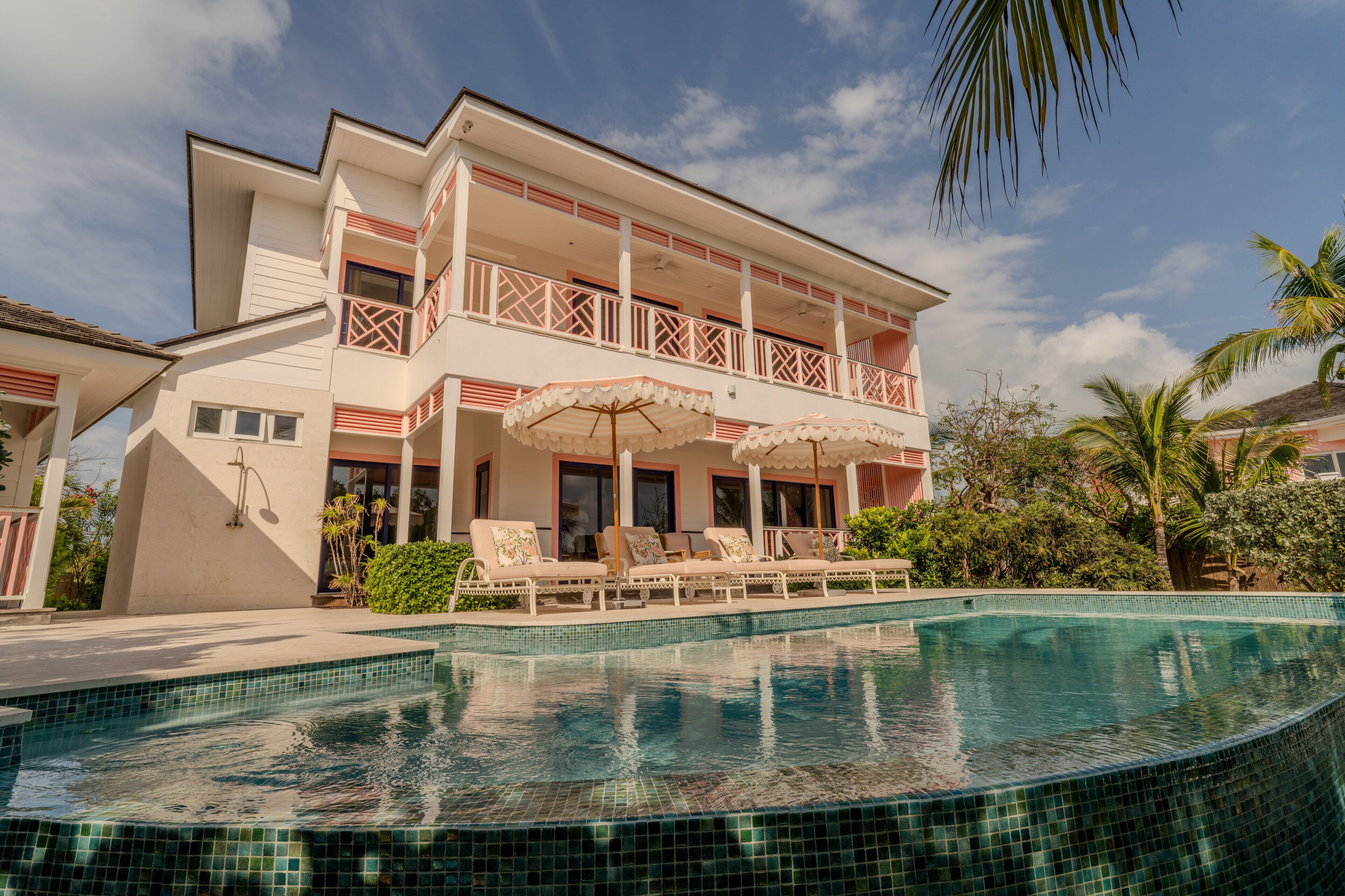 A two-story building with a swimming pool, outdoor lounge chairs, and umbrellas.