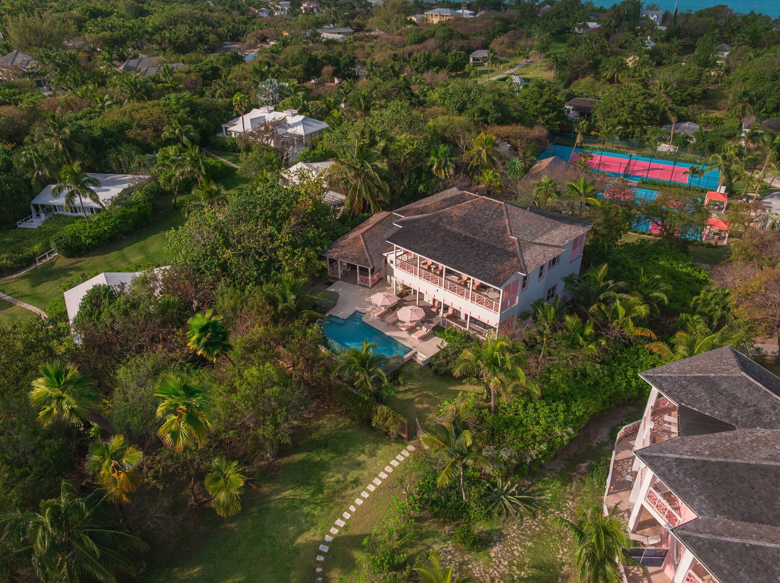 Une vue aérienne d’une grande maison avec une piscine, entourée d’une végétation luxuriante et d’autres habitations.