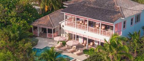 A large house with a pool, surrounded by lush greenery and palm trees.