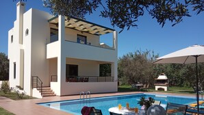 Ein modernes, zweistöckiges Haus mit Swimmingpool, Sitzgelegenheiten im Freien und Grillplatz.