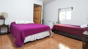 A bedroom with two beds, a wooden door, a window, and a bedside table with a lamp. - Casita happy feet and tours corcovado - Family Room with Garden View (Bahía Drake)
