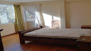 A bedroom with a wooden bed, a wooden nightstand, a chair, and a window with curtains.