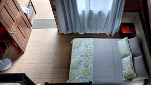 A bed with a floral bedspread, a bedside table with a lamp, and a window with curtains. - Casita happy feet and tours corcovado - bedroom #6 (Drake Bay)