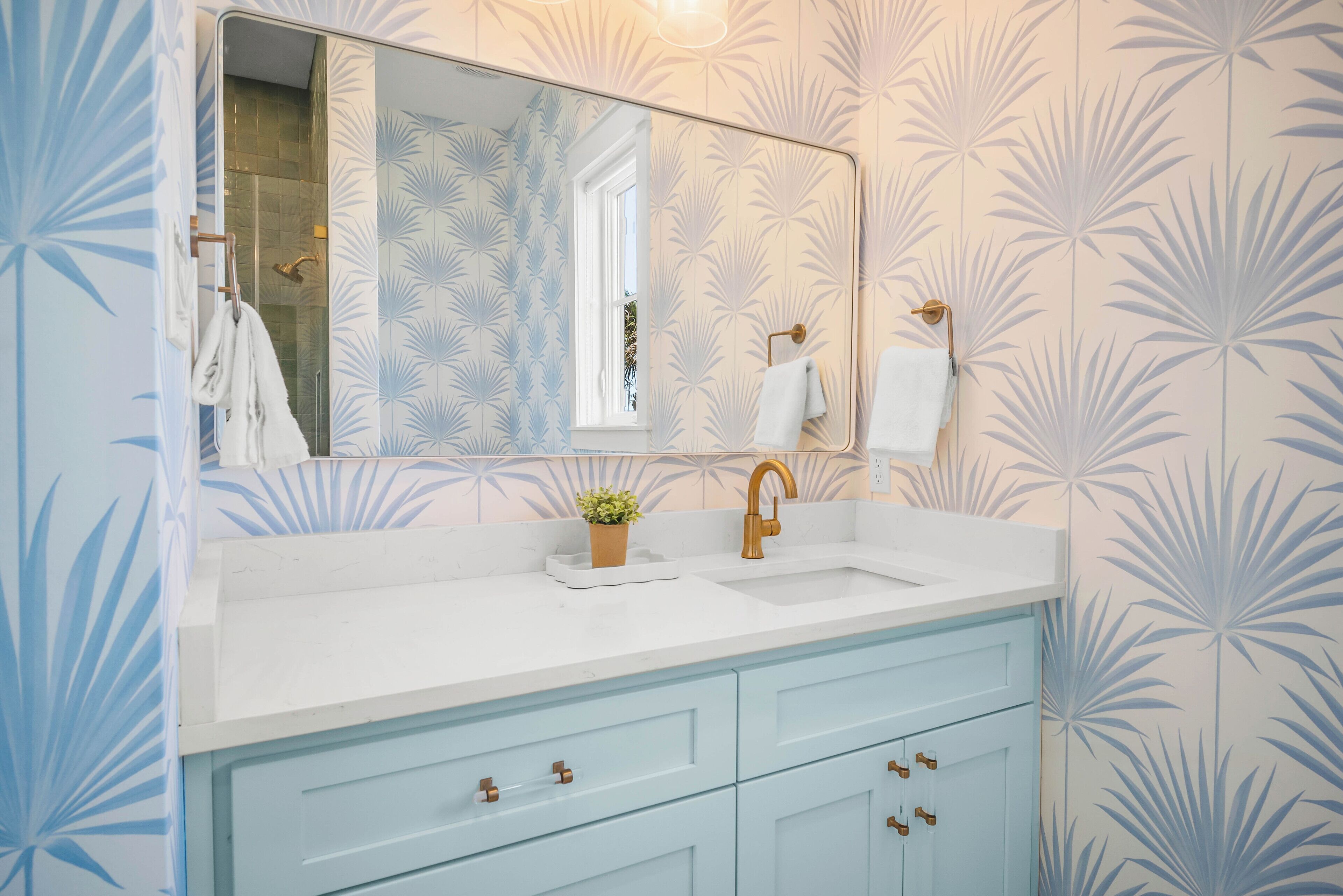 Une salle de bain avec un lavabo blanc, un grand miroir et des meubles de couleur bleu clair.