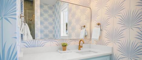 Une salle de bain avec un lavabo blanc, un grand miroir et des meubles de couleur bleu clair.