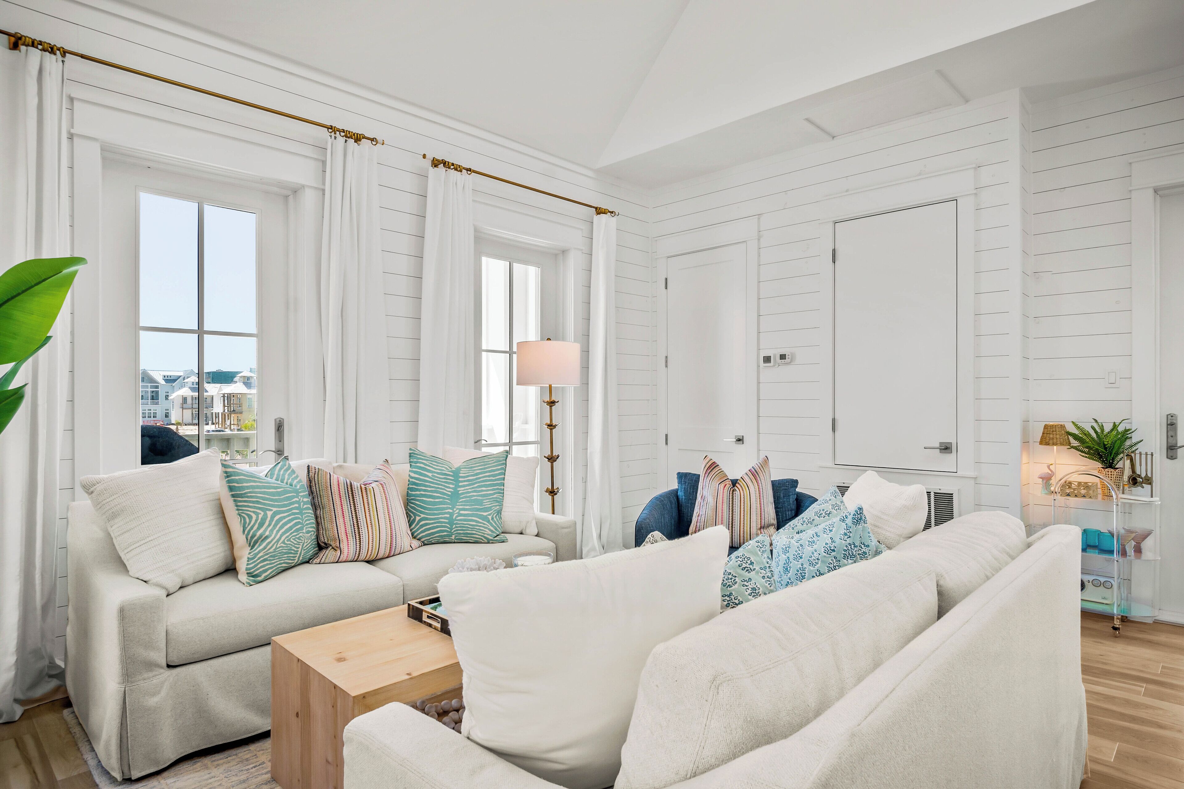 Un salón moderno con muebles blancos, un ventanal con cortinas y vistas a la ciudad.