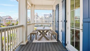 A covered porch with a wooden table and benches, a view of neighboring houses, and a blue door. - Let's "glow" Girls 113 Tai-d (Port Aransas)