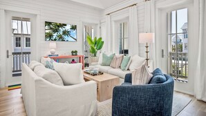 A spacious living room with a white color scheme, a wooden coffee table, and a view of the outdoors through large windows. - Let's "glow" Girls 113 Tai-d (Port Aransas)